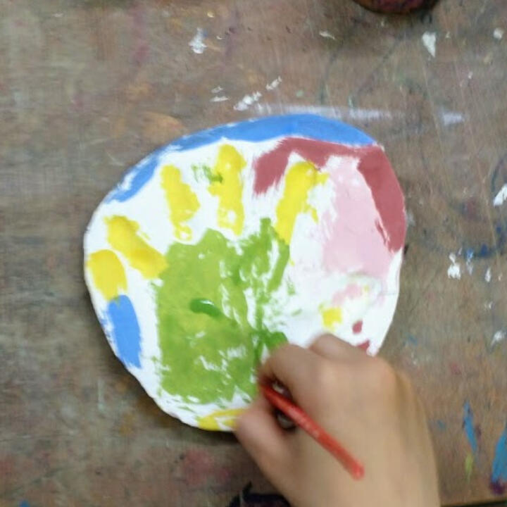 Close up of a child's hand while painting a ceramic imprint of their own hand