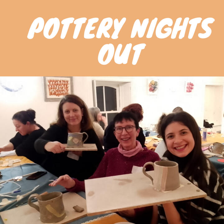 Three women smiling and showing their unfired clay mugs made during a pottery workshop